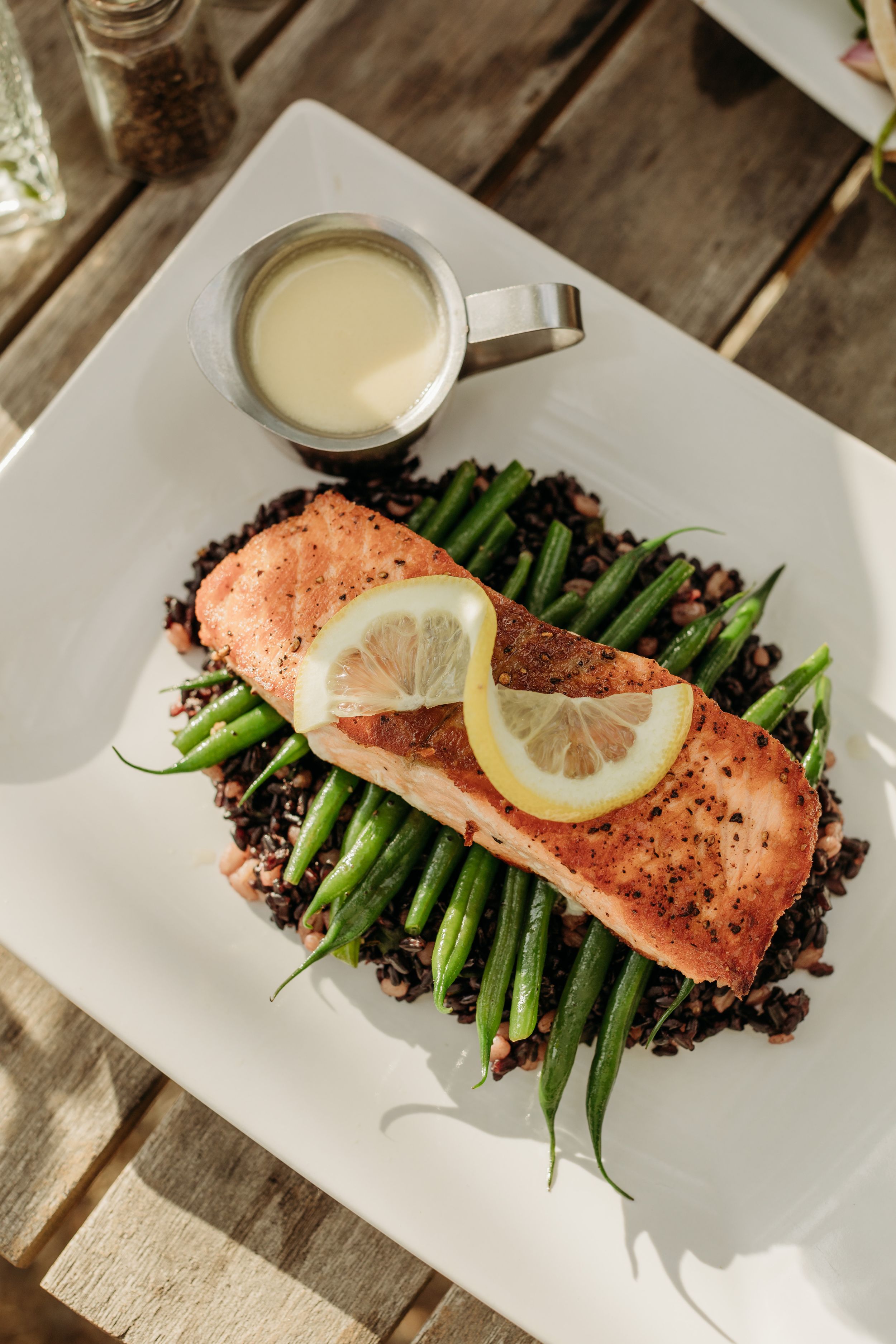Grilled salmon fillet served with asparagus on black rice and a lemon slice with cream sauce.