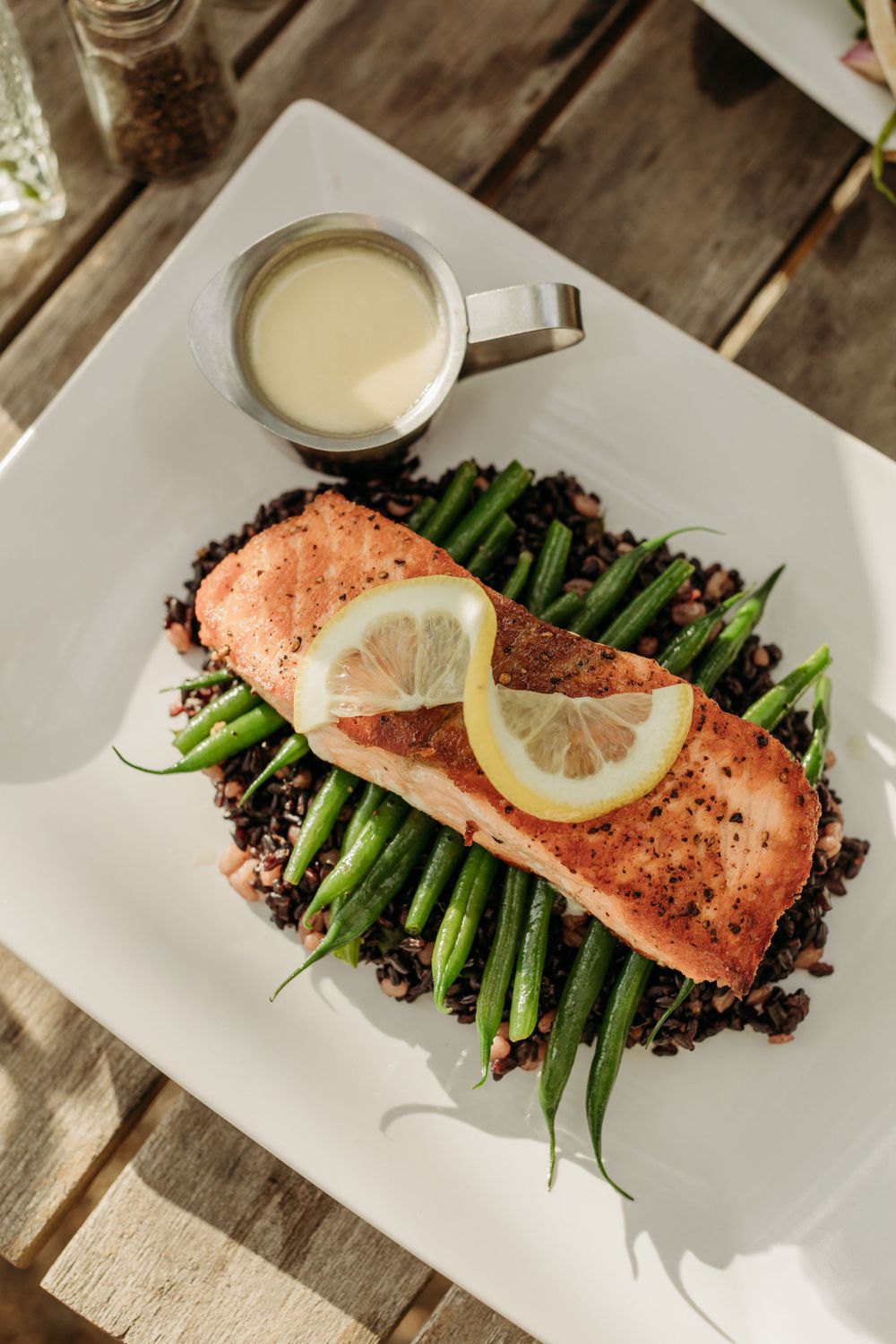Grilled salmon fillet served with asparagus on black rice and a lemon slice with cream sauce.