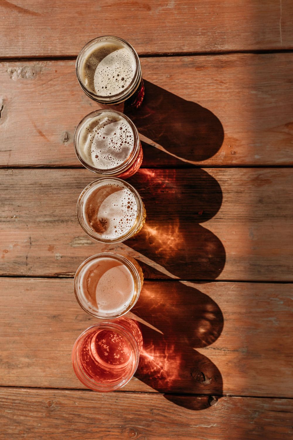 Five different craft beers arranged diagonally on wooden surface showing color gradient.