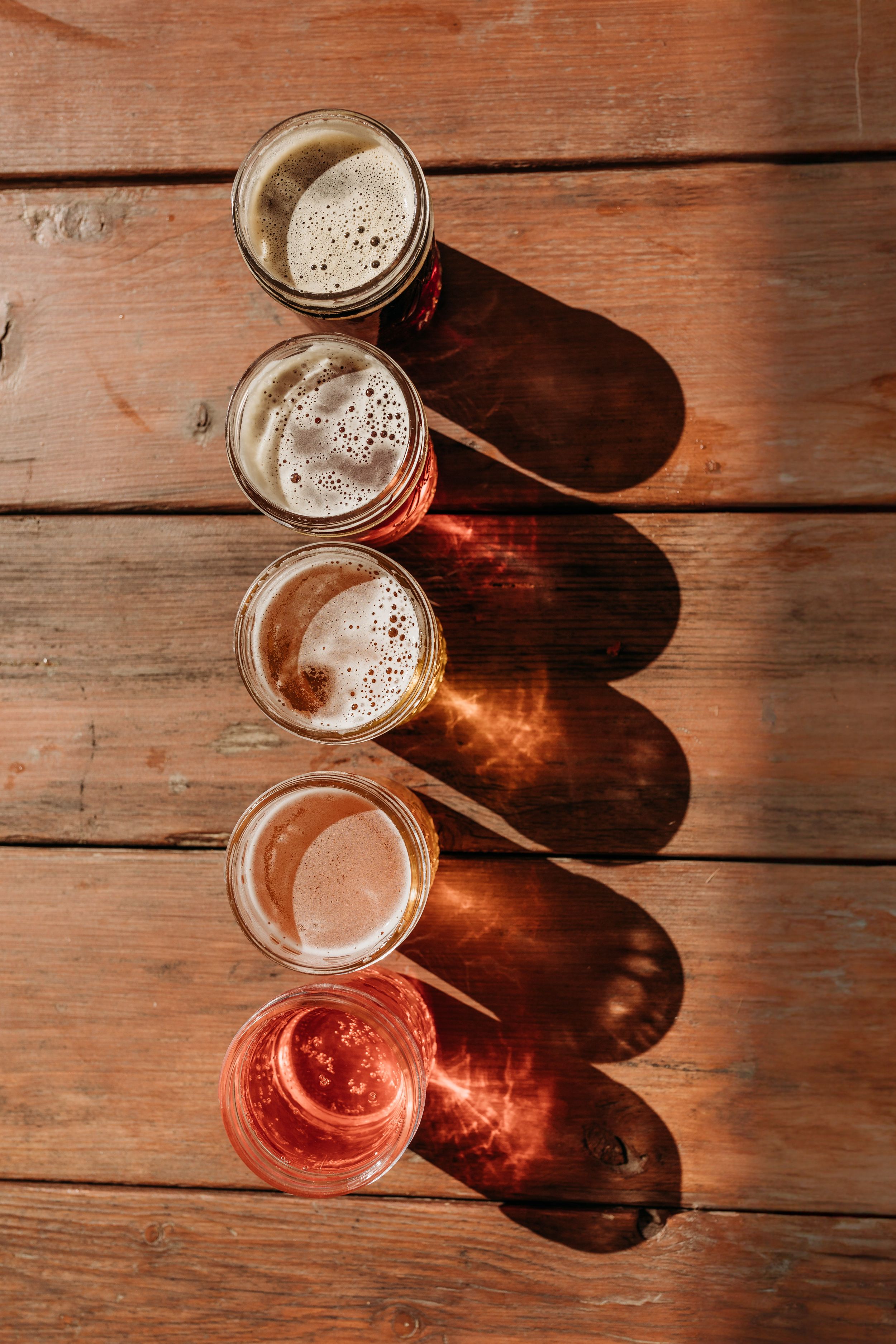 Five different craft beers arranged diagonally on wooden surface showing color gradient.