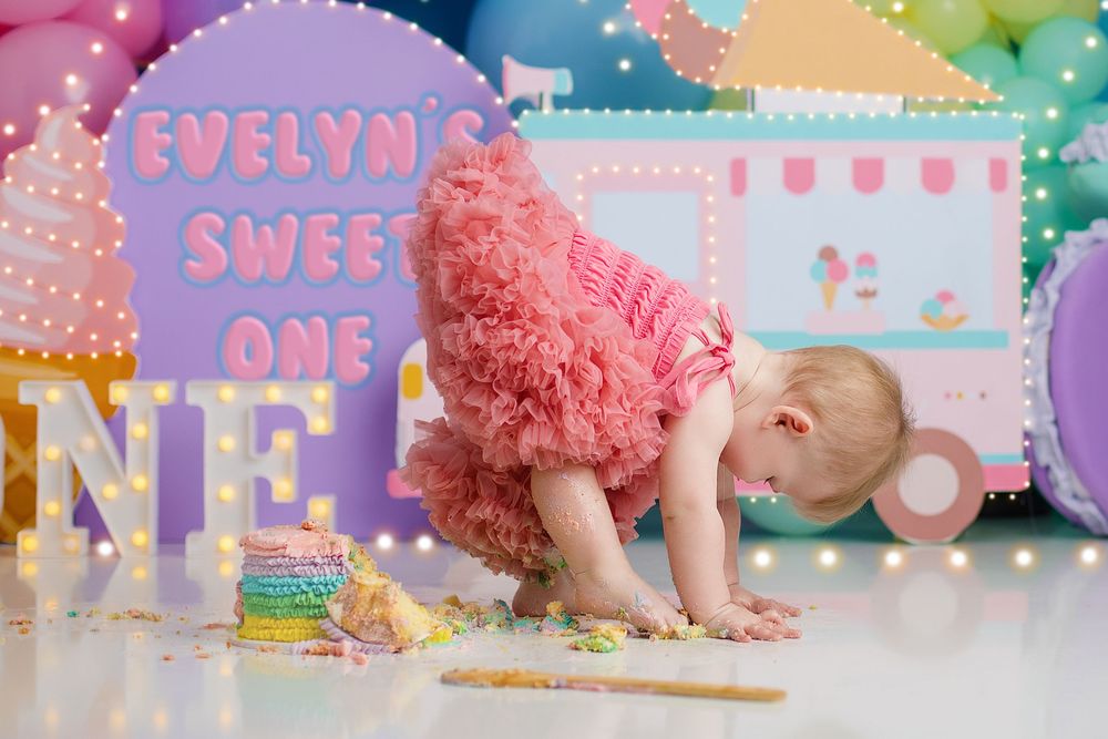 Festive cake smash photo with rainbow balloons and pink ice cream truck theme party decorations. wardrobe and outfits included.