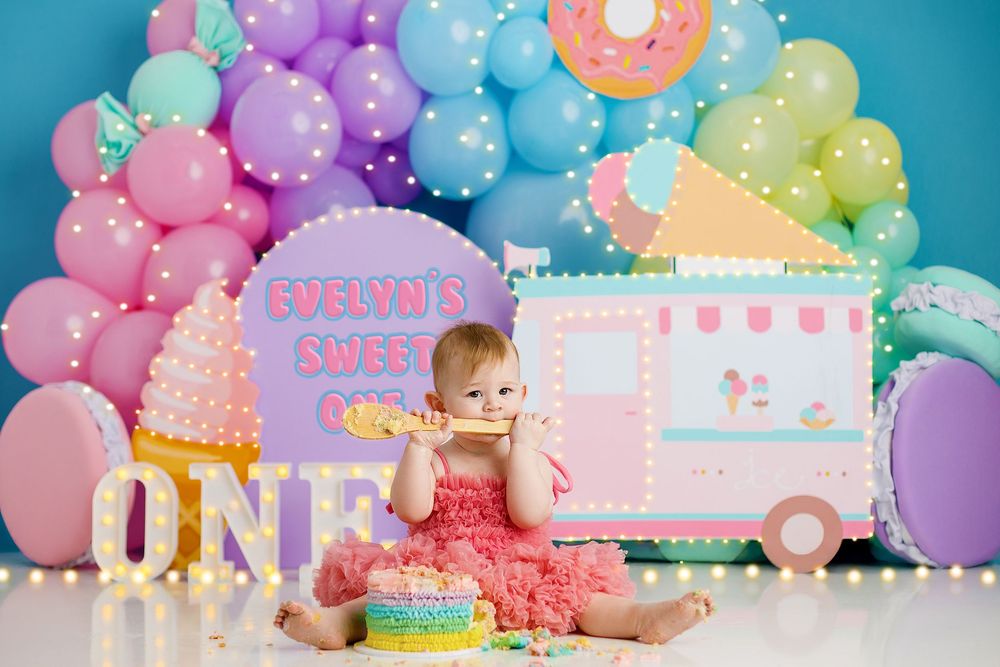 Colorful first birthday party setup with balloon arch, cake smash scene and pink ice cream truck backdrop. brookwater, yummy cake.