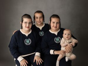 Family portrait with matching navy blue sweaters against dark grey background.