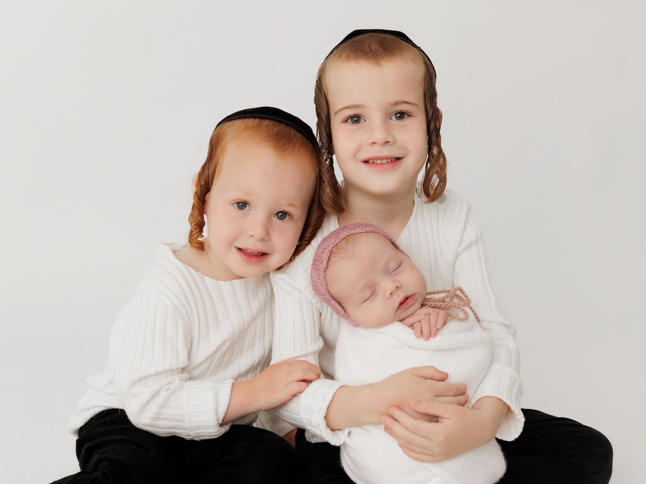 Three siblings in white tops sitting together against light background.