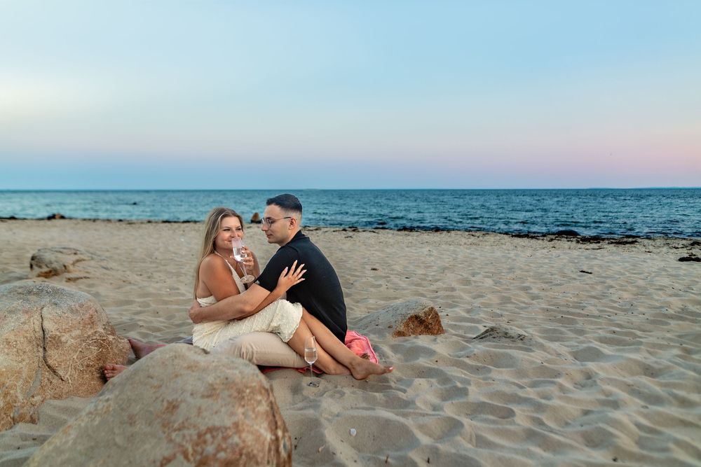 A couple enjoys a romantic moment on a sandy beach at sunset with ocean waves in the background.