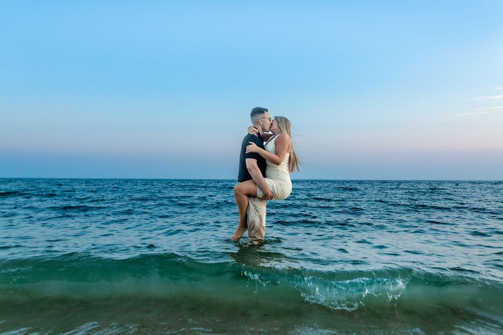 A couple embraces during a romantic beach photoshoot in the ocean at sunset.
