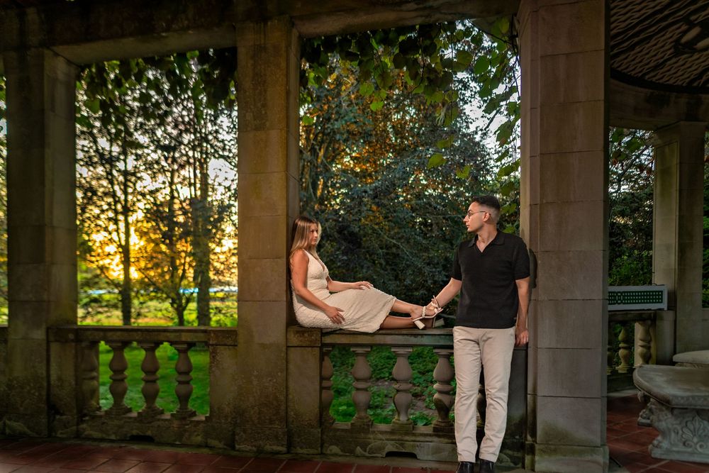 A couple shares a tender moment at sunset on an elegant stone balcony surrounded by lush greenery.