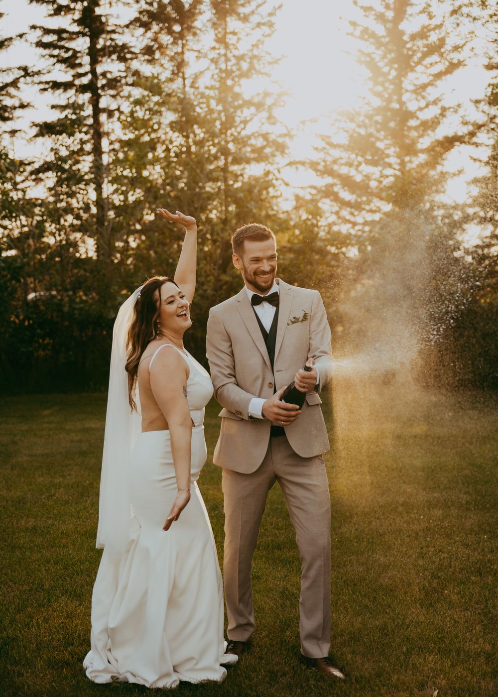 Wedding couple laughing together on grass at Hillside Acres wedding venue in during golden hour with sunlight filtering through trees.