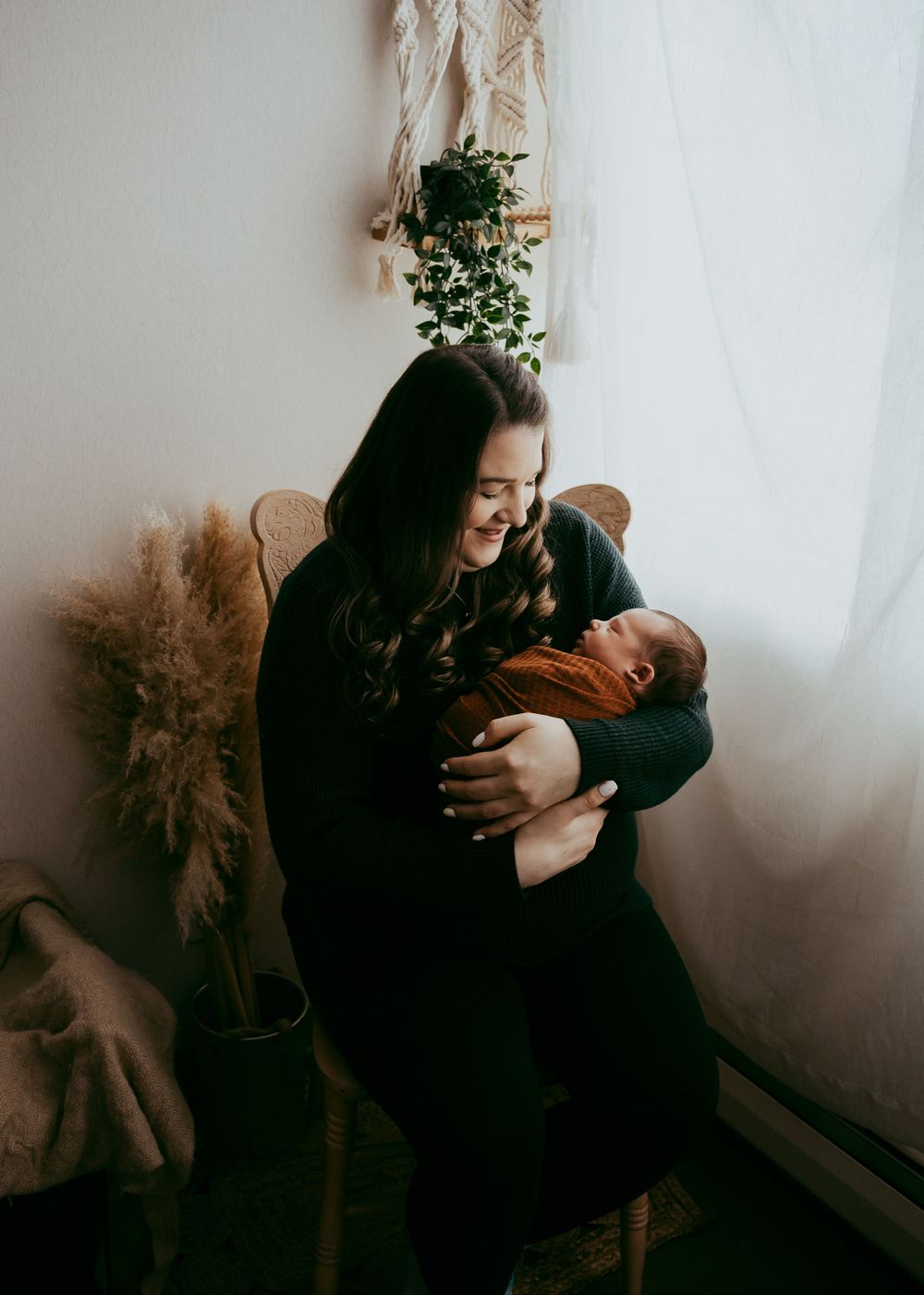 Tender moment between parent and baby in moody indoor studio setting in Fort Saskatchewan with dried flowers.
