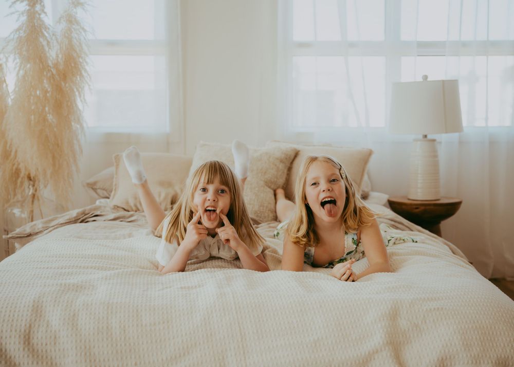 Playful scene of children jumping on white bed with natural window light.