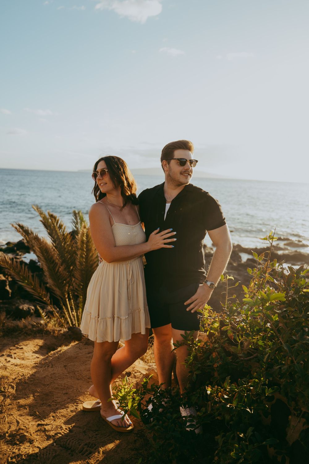Couple posing together on a scenic coastal cliff in Hawaii with pampas grass during golden hour.