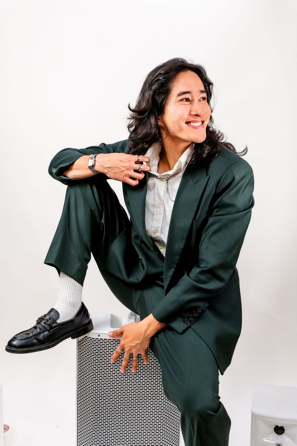 Dj and Real Estate man Dj Can Nguyen sits on top of a speaker in a green suit holding the inside of the blazer and turning his head right