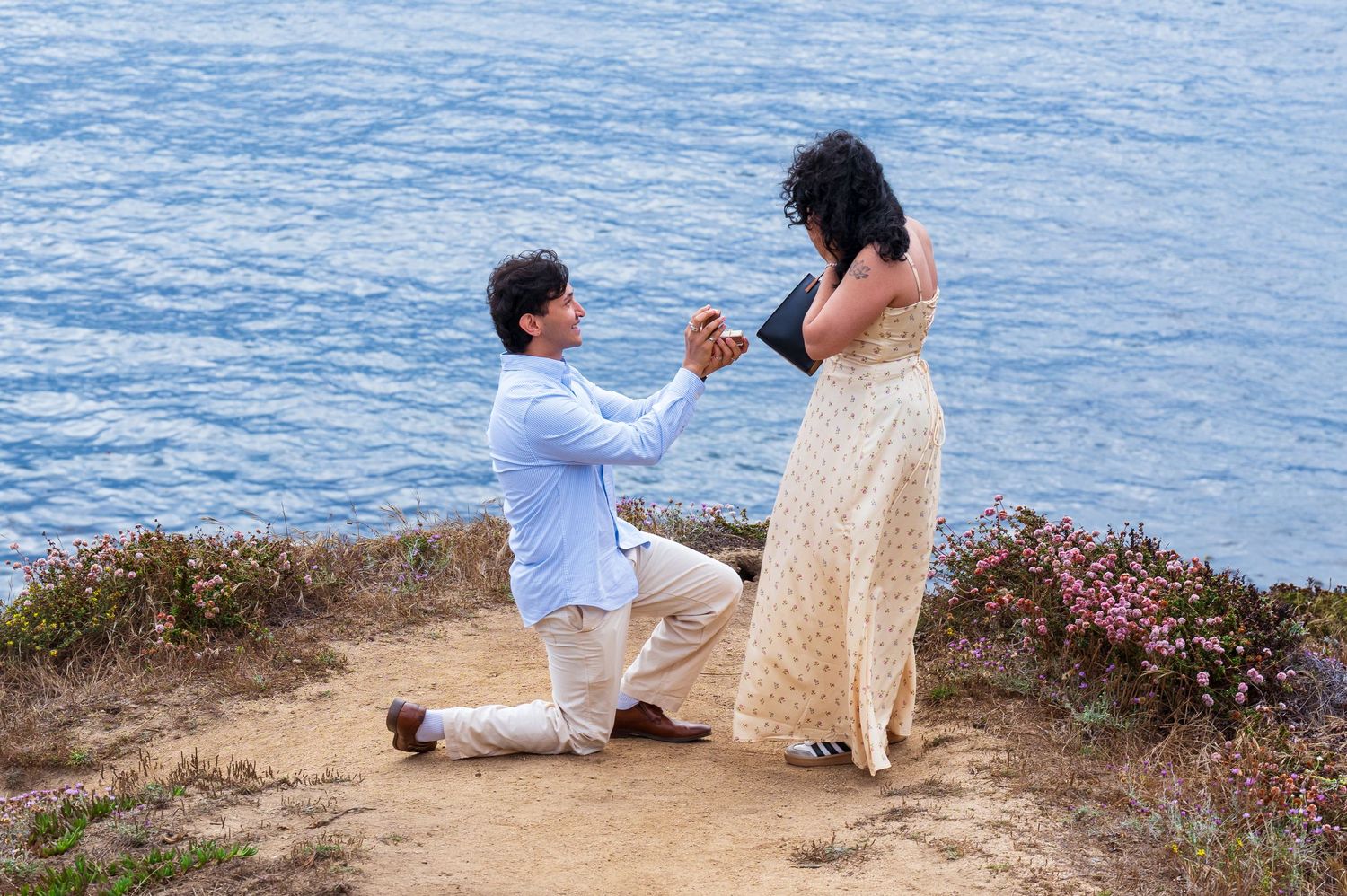 A photo of a man getting down on one knee to propose to his girlfriend to make her his fiancee. Beach proposal photo shoot in Garrapata park