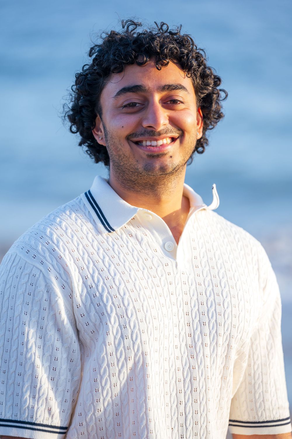 Environmental portrait of a man in a white polo with blue accents at Leo Carrillo State Beach. He has curly hair
