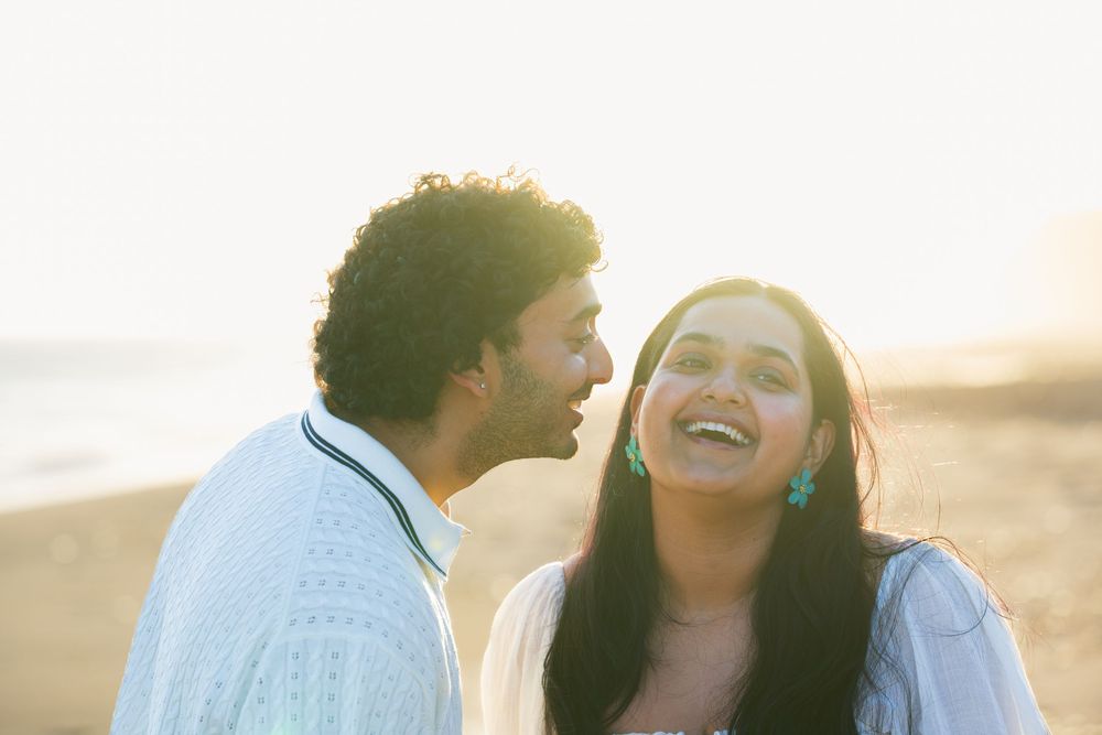 A cute couple photo taken at Leo Carrillo State Beach during sunset. The man leans in to kiss the lady's cheek while she laughs