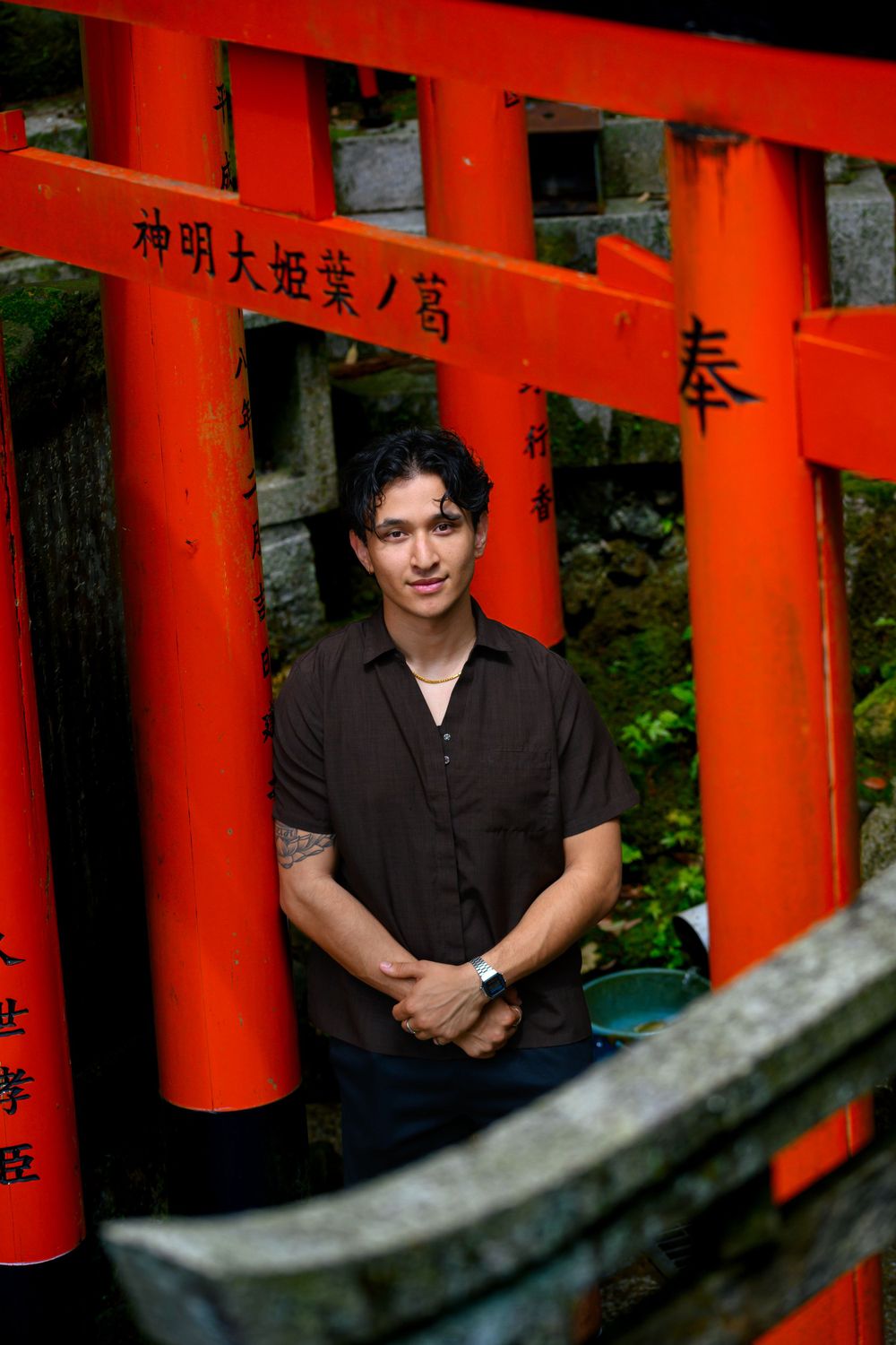 An environmental portrait of a man in a brown shirt standing in the center underneath tori shrines in Japan. The tori shrines frame the man.