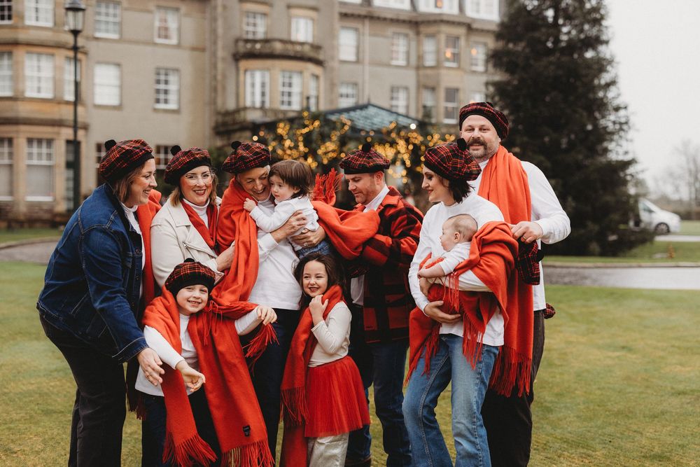 A joyful family group in matching red scarves and festive hats poses outdoors near a grand building.
