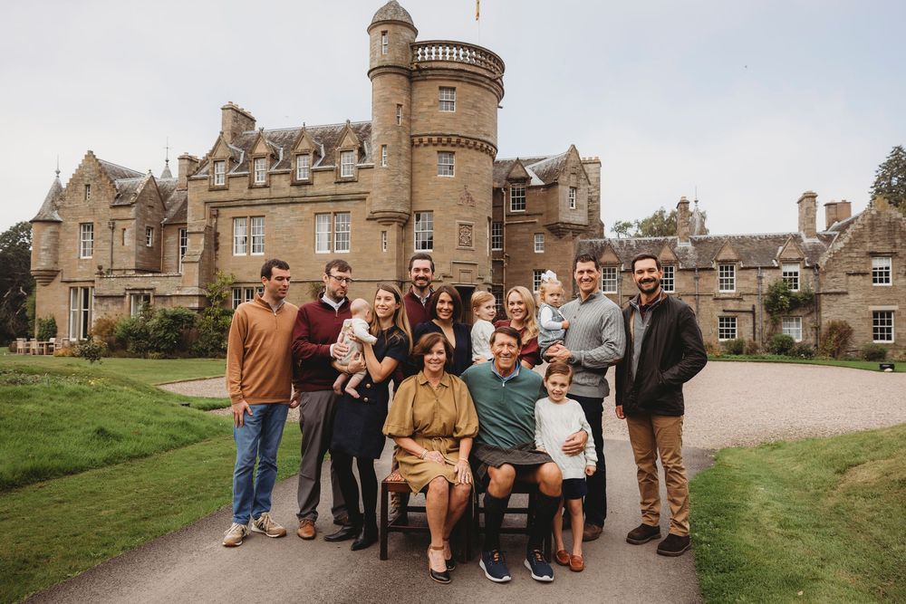 Large family group posing in front of a grand Scottish castle surrounded by lush green grounds.