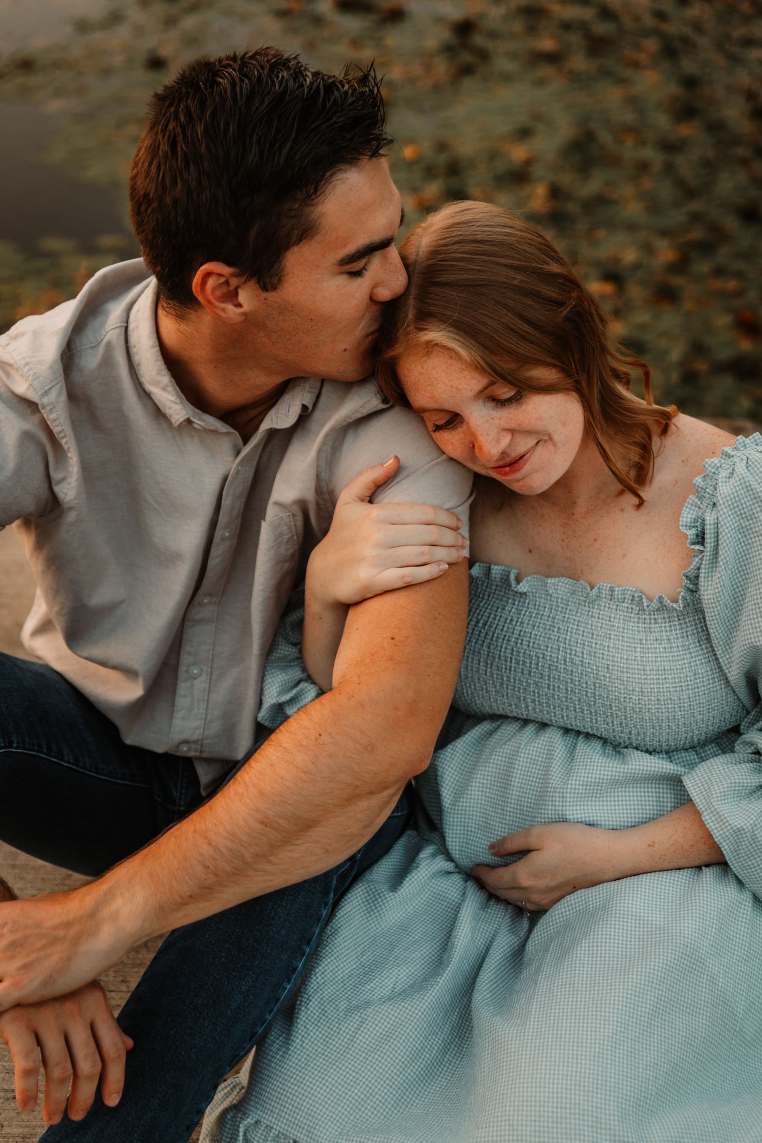 An intimate maternity photo showing a couple in soft lighting with her wearing a blue dress.