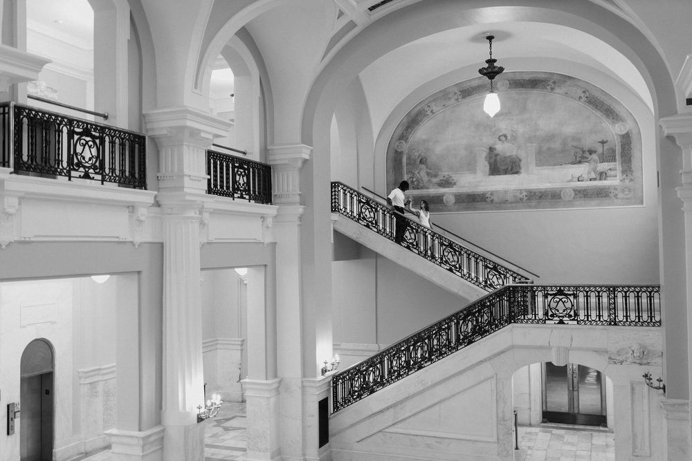 a young couple walks down a staircase in a massive marble museum