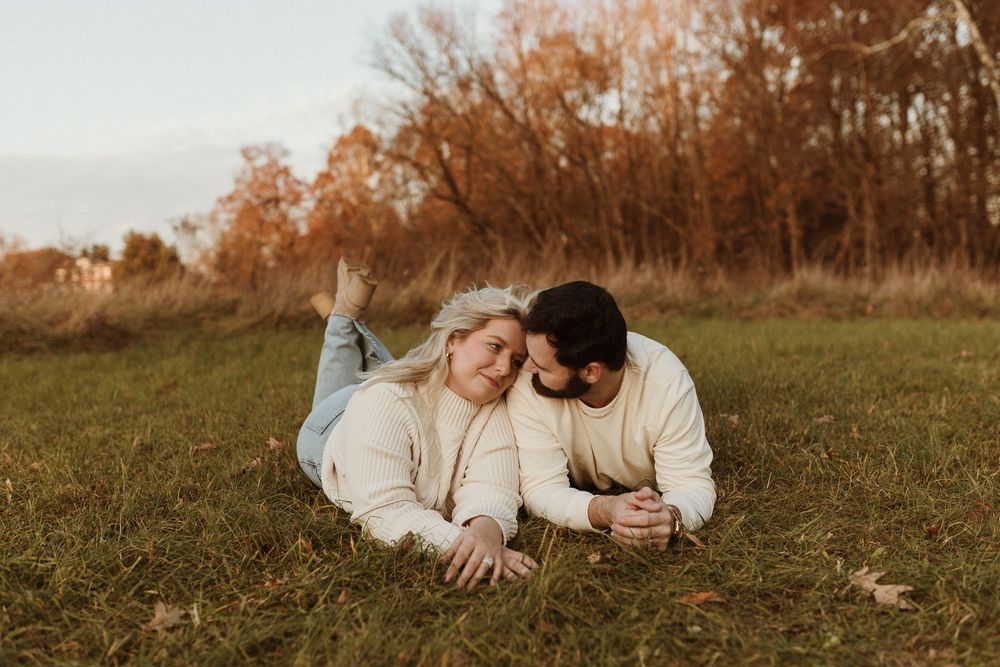 a couple laying close together in an open field, the female laying her head on the mans shoulder and looking into his eyes.