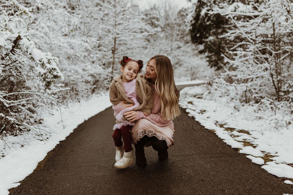 a mother sits her young daughter on her lap in a snowy scene