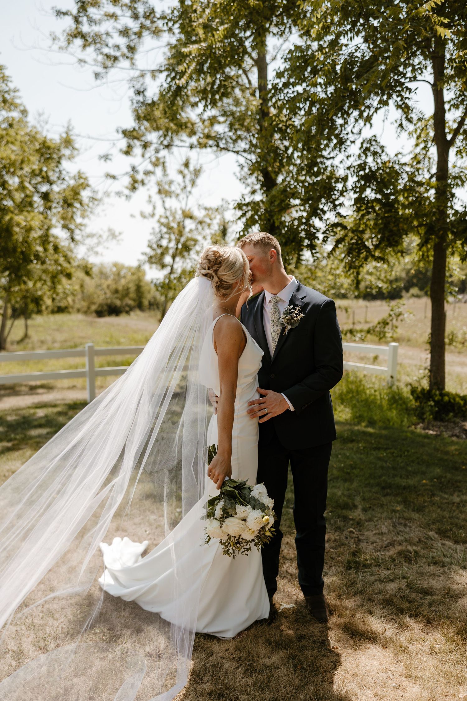 A bride and groom embrace in a scenic outdoor setting with trees and greenery surrounding them. Fort Worth Texas wedding photographer.