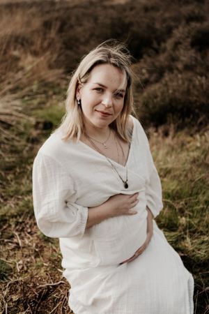 Zwangere vrouw houdt haar buik vast en kijkt in de camera tijdens een zwangerschapsshoot