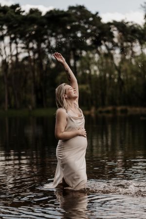 Creatieve foto van zwangere vrouw in het water terwijl ze haar buik vasthoudt