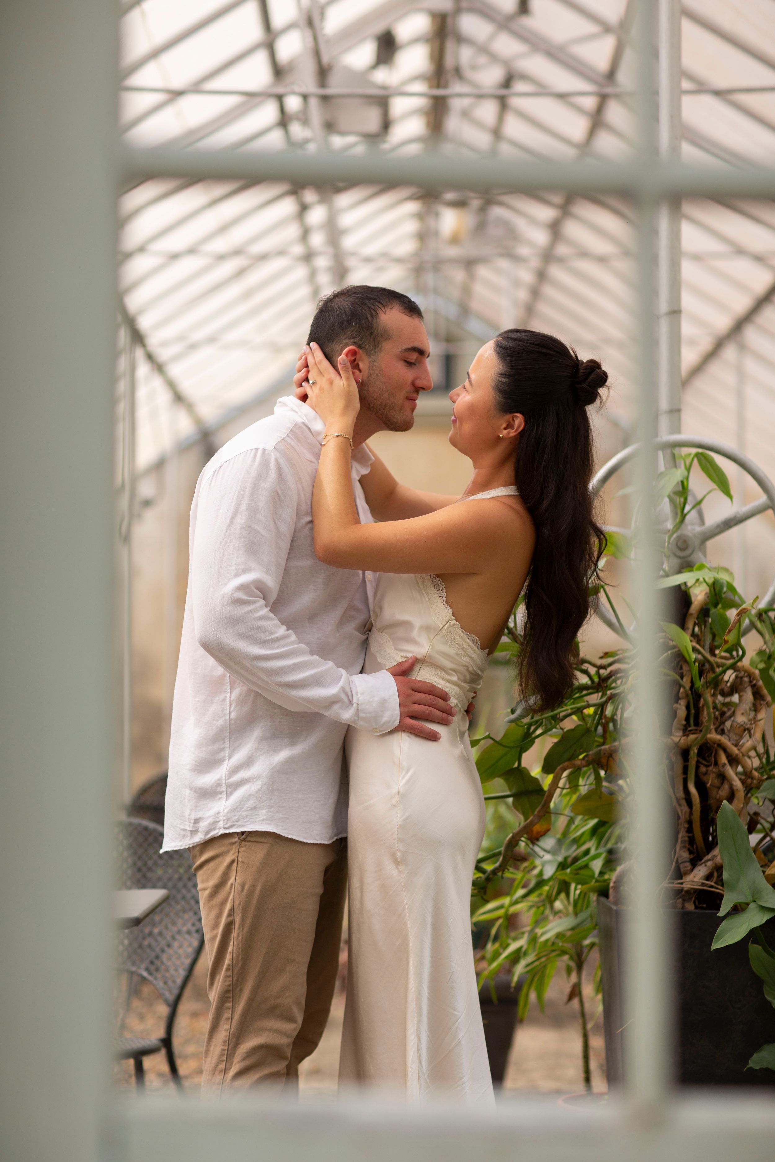 Couple shares an intimate embrace inside a lush greenhouse on their wedding day.
