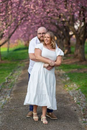 Happy couple embracing on a path lined with blooming pink cherry blossom trees.