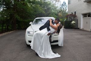 Bride and groom sharing a romantic dip kiss in front of a white Rolls-Royce.