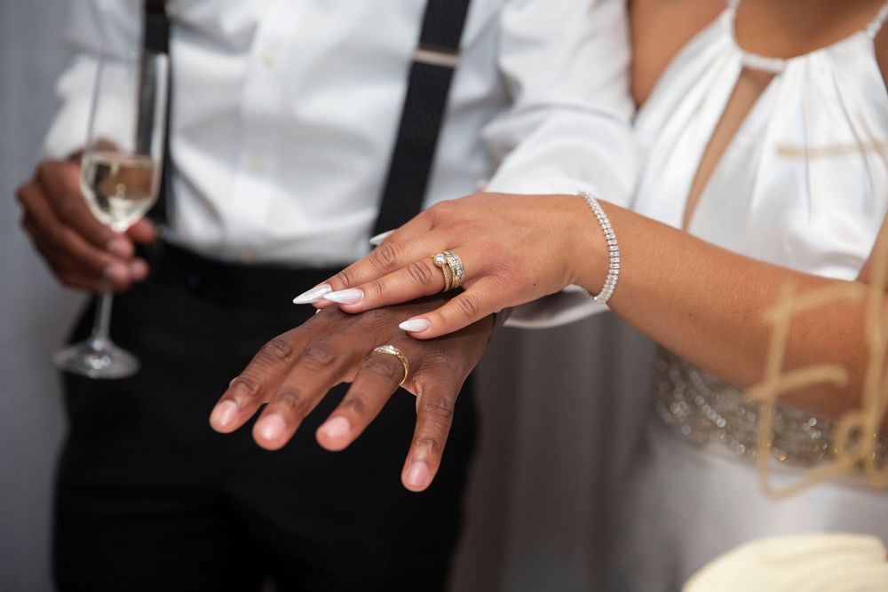 Close-up of newlyweds hands showing wedding rings, bride holding champagne glass.