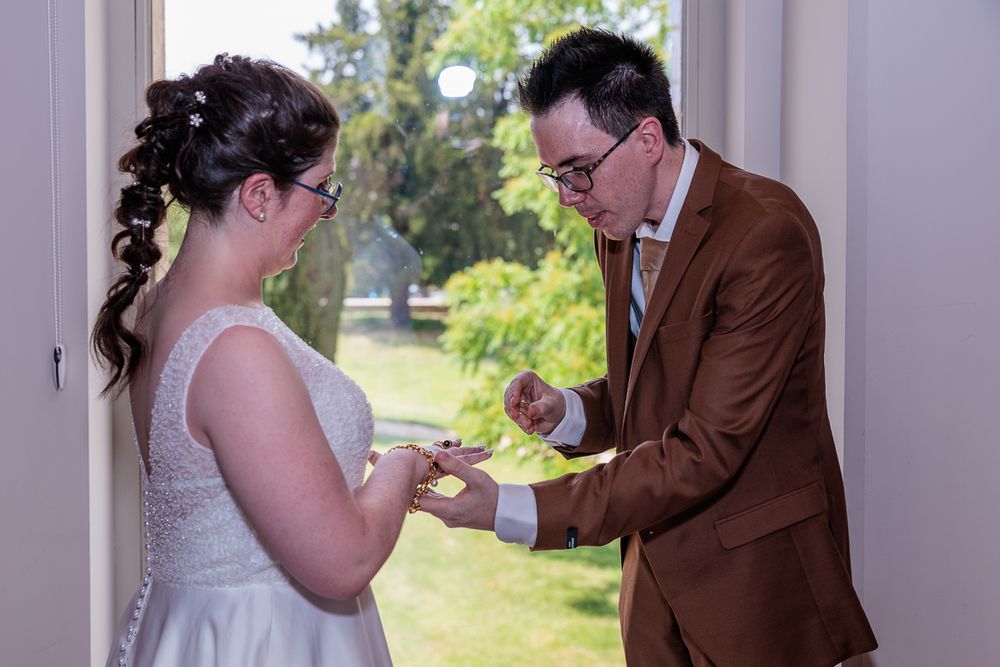 Bride and groom exchanging wedding rings indoors, with lush green garden visible through open door.