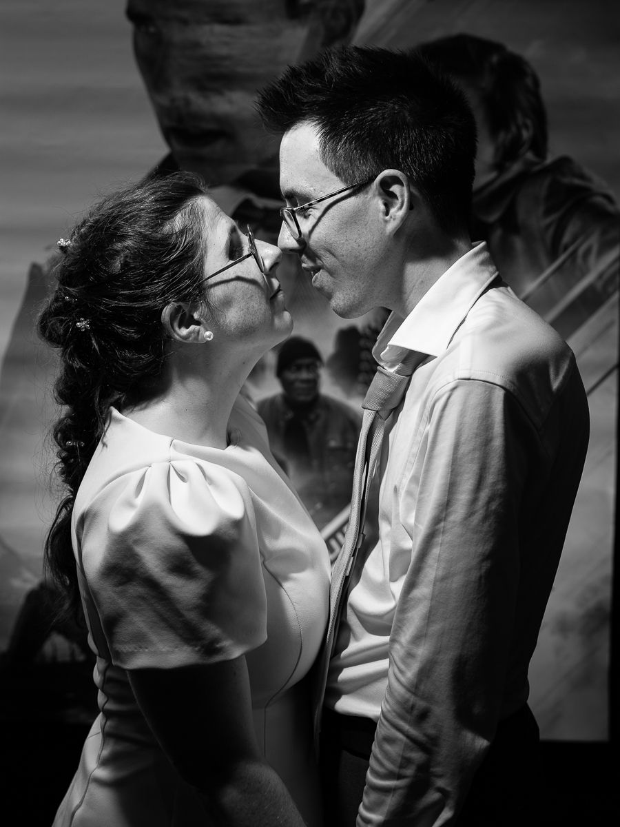 Black and white photo of a couple in glasses sharing a romantic moment, nearly kissing at a formal event.