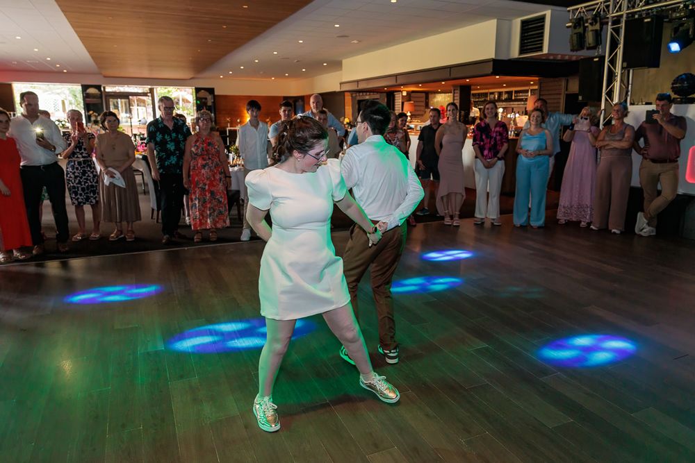 Couple dancing energetically on illuminated dance floor at wedding reception with guests watching.