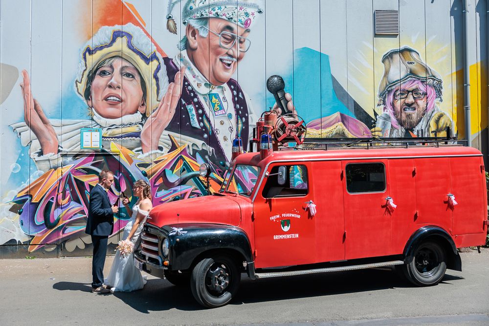 Vintage red fire truck parked in front of a vibrant colorful mural featuring festive costumed figures.