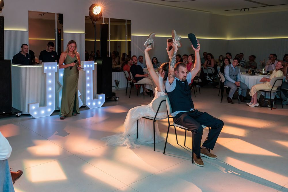 Bride and groom perform fun chair dance at wedding reception with illuminated letter decorations.