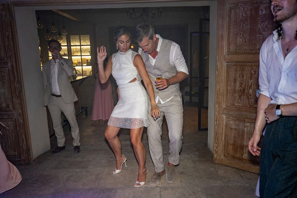 A couple in light colored wedding attire dance close together on a dimly lit dance floor at an evening celebration.