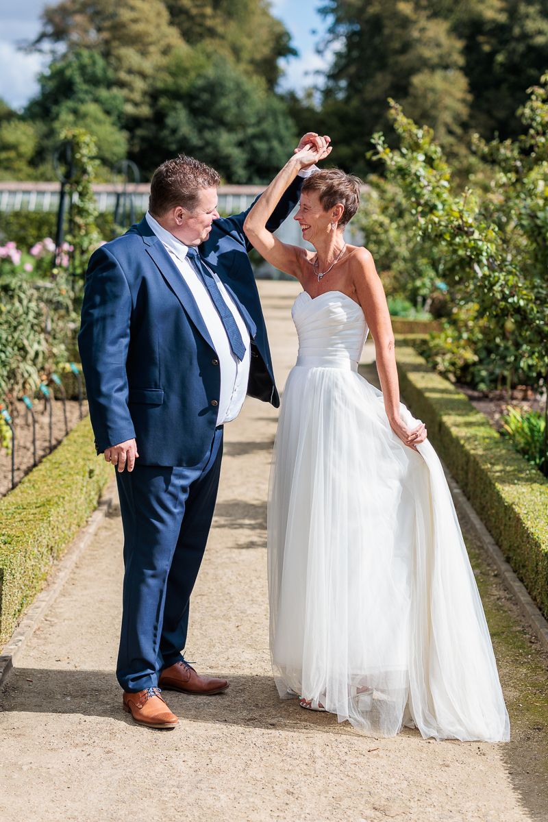 Bride and groom dancing together in a beautiful garden, with the bride in a white gown and groom in a navy blue suit.