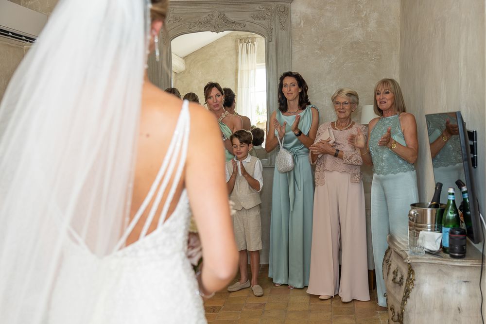 Bridesmaids in pastel dresses react emotionally as they see the bride in her wedding gown for the first time.