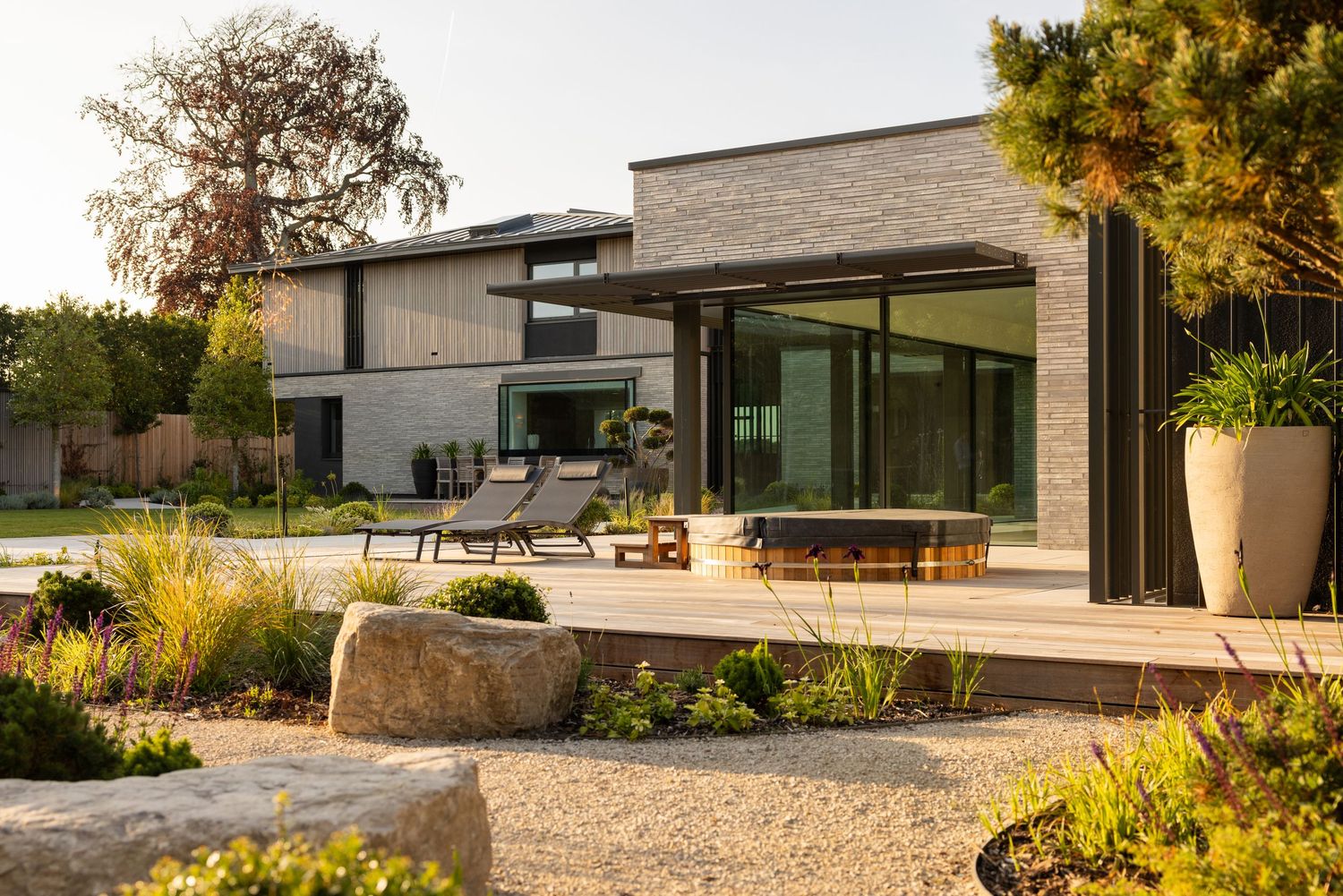 Luxurious gray shingle-style mansion with symmetrical architecture and rectangular pool in front.