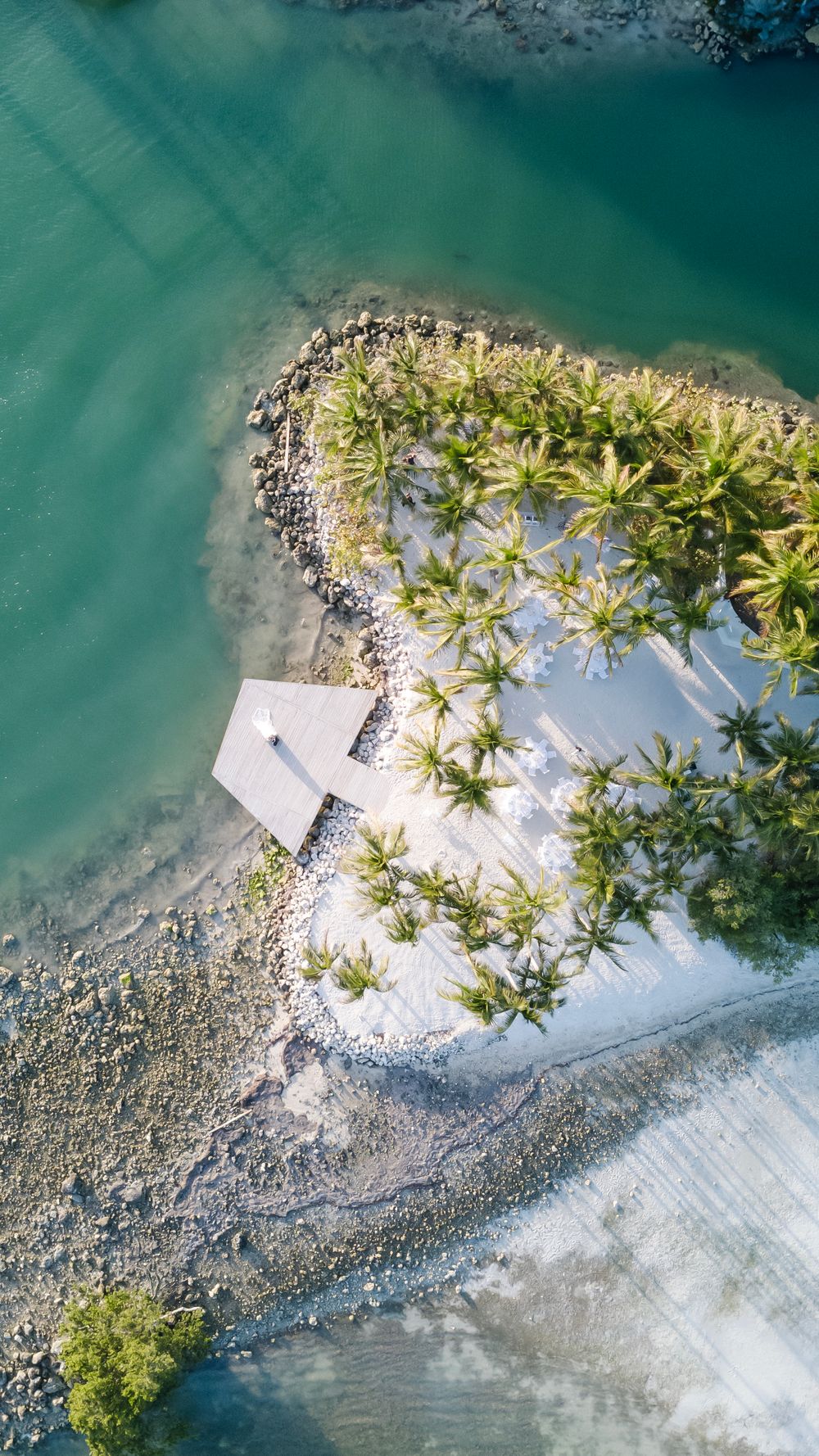 Aerial drone view of a tropical island with white sand beach, palm trees, and turquoise ocean waters.