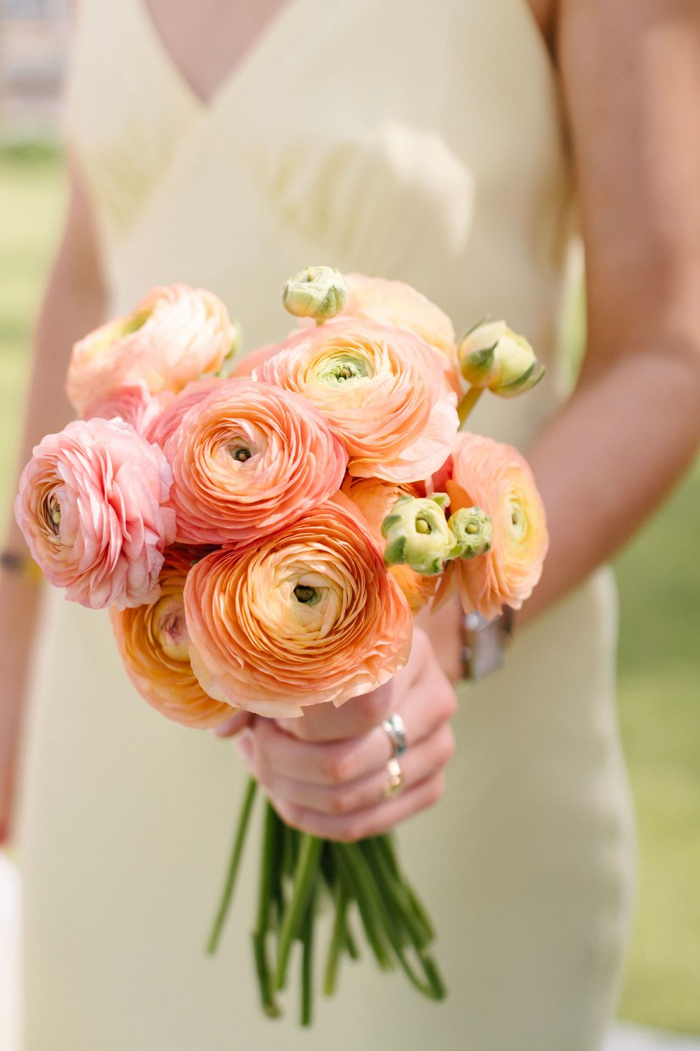 Bridesmaid in yellow dress holding a lush peach and pink ranunculus wedding bouquet.