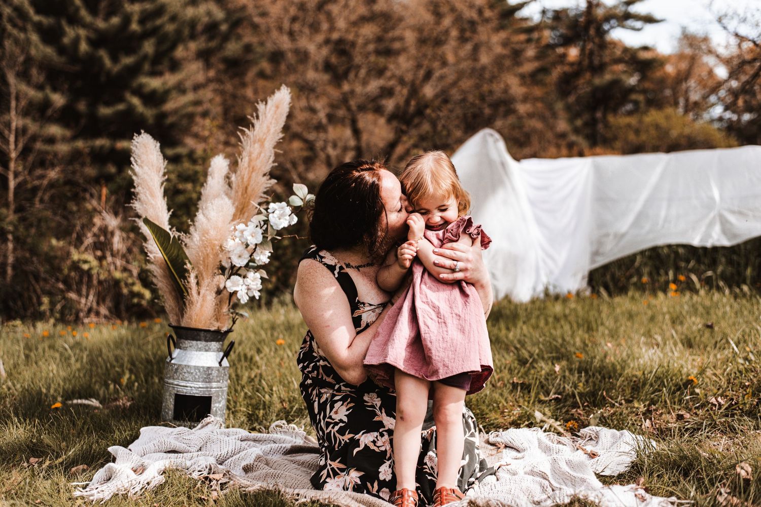 An outdoor portrait features floral arrangements with pampas grass and special moments on a picnic blanket.