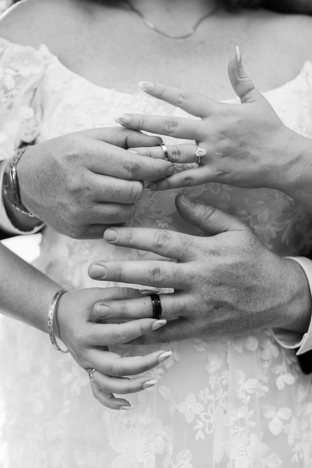 Close-up black and white photo of bride and groom displaying wedding rings on hands.