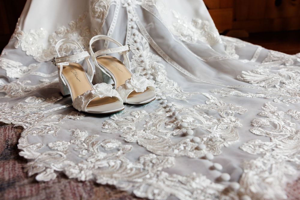 Elegant bridal heels with floral embellishments resting on intricate lace wedding dress fabric.