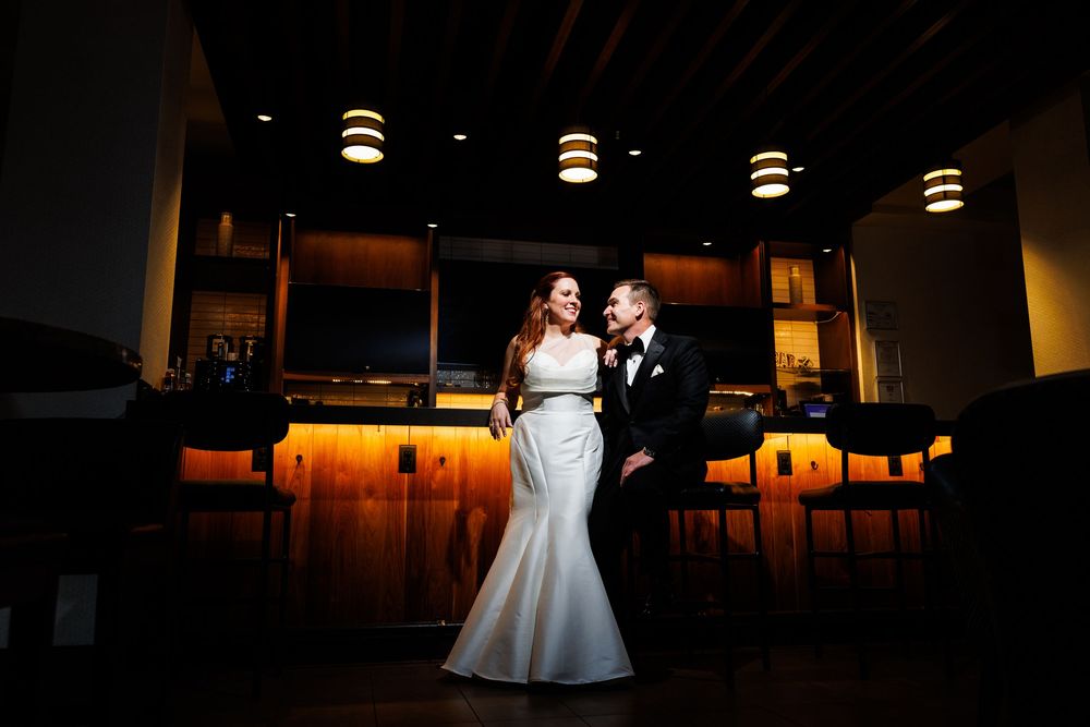 Bride and groom share a romantic moment in front of a glowing bar at their elegant wedding reception venue.