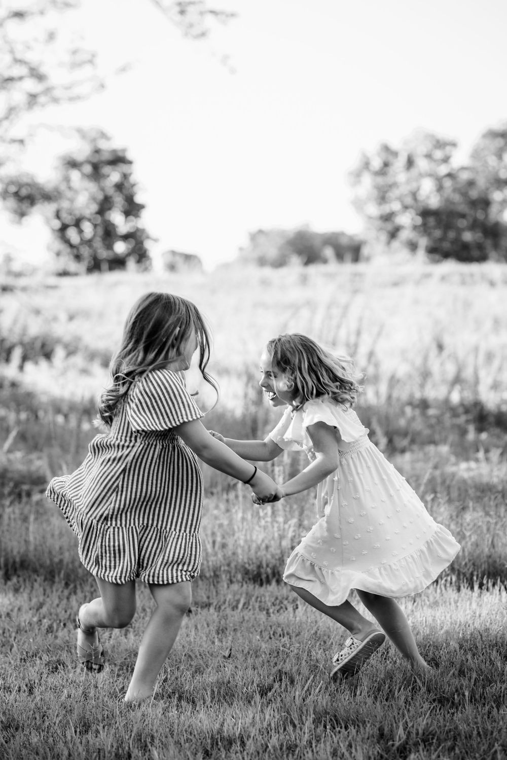 Black-and-white photo of two sisters running through a field during a family reunion session in Mountain Home, Arkansas