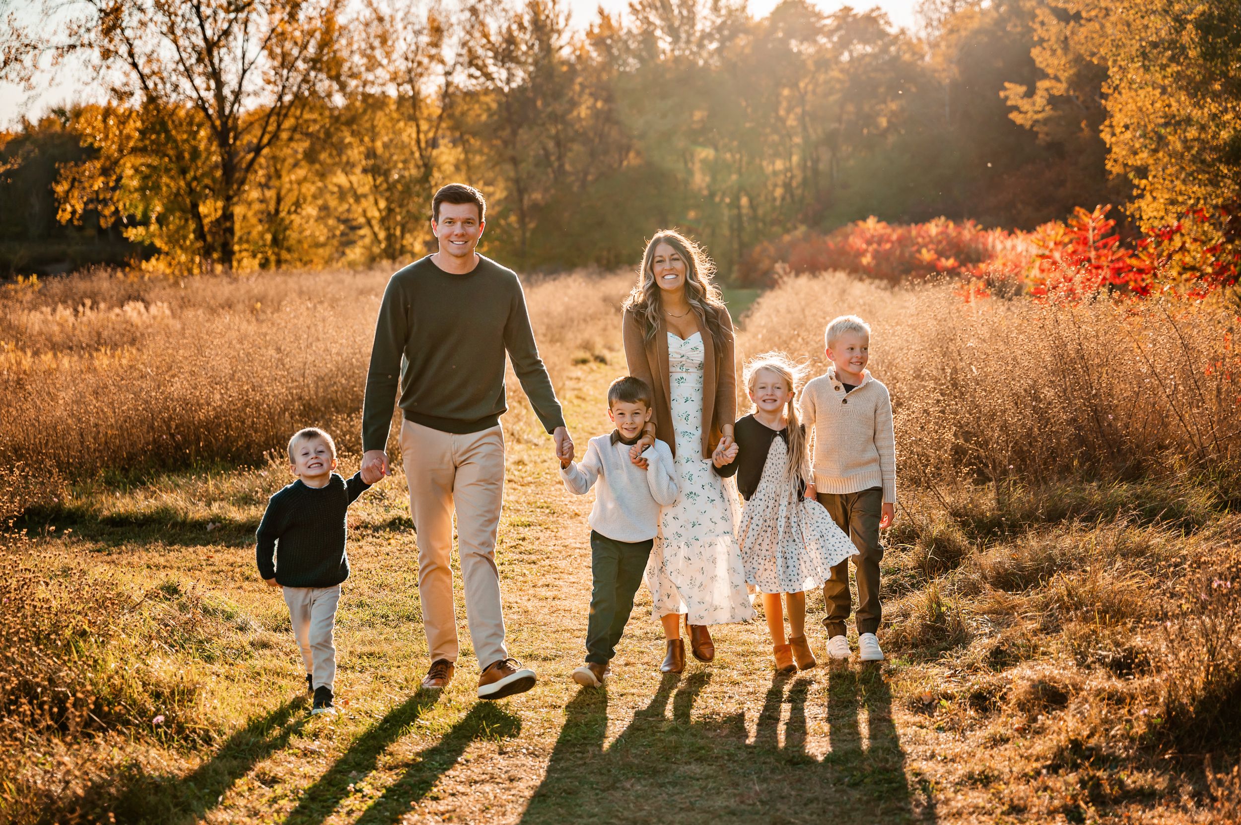 Family of five walking together on path during golden hour in autumn setting.
